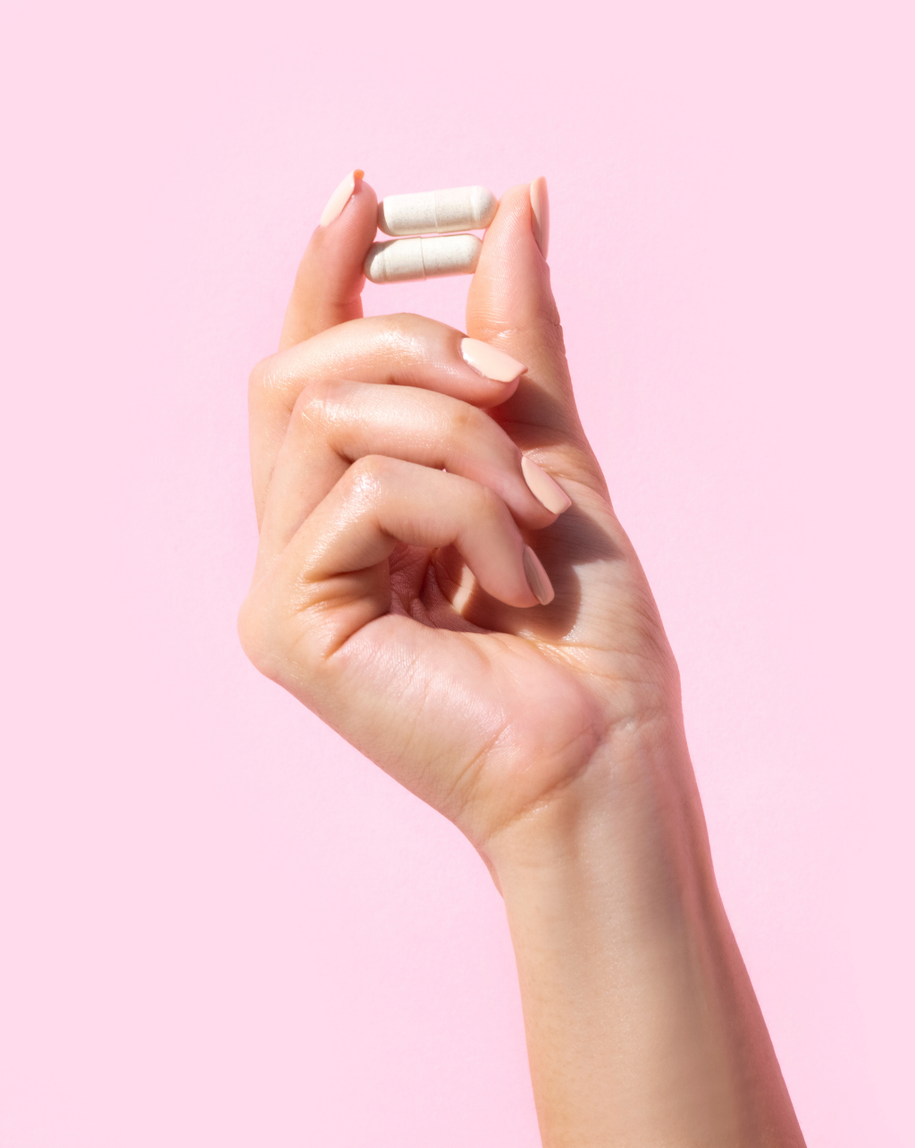Femme hand holding two TAKE N GO™ Daily Hair & Scalp Vitamins against a pale pink background.